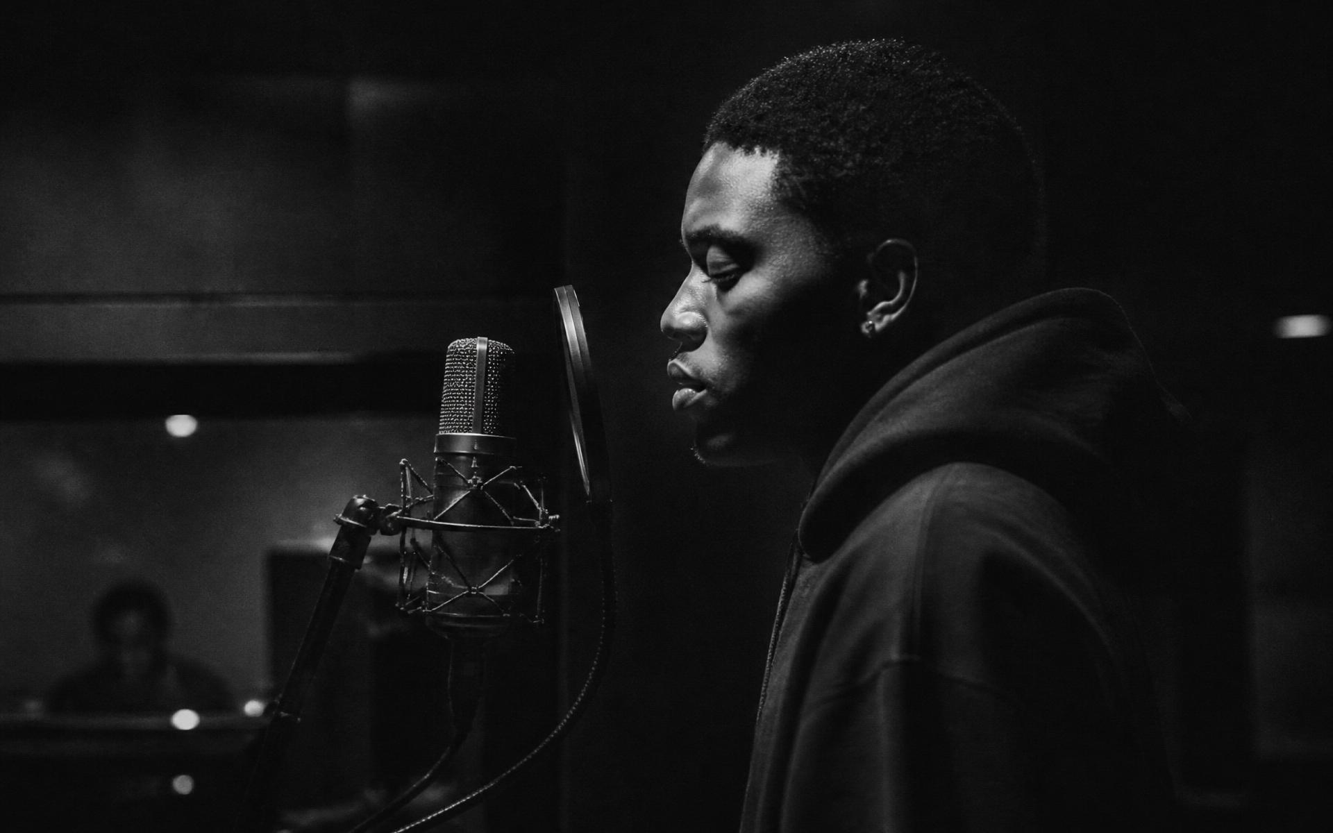 An artist at the microphone, mid-take, in a darkened studio
